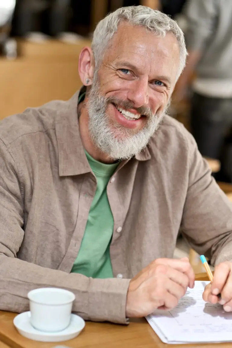 Happy old man professor writing in notebook sitting at table. Vertical portrait